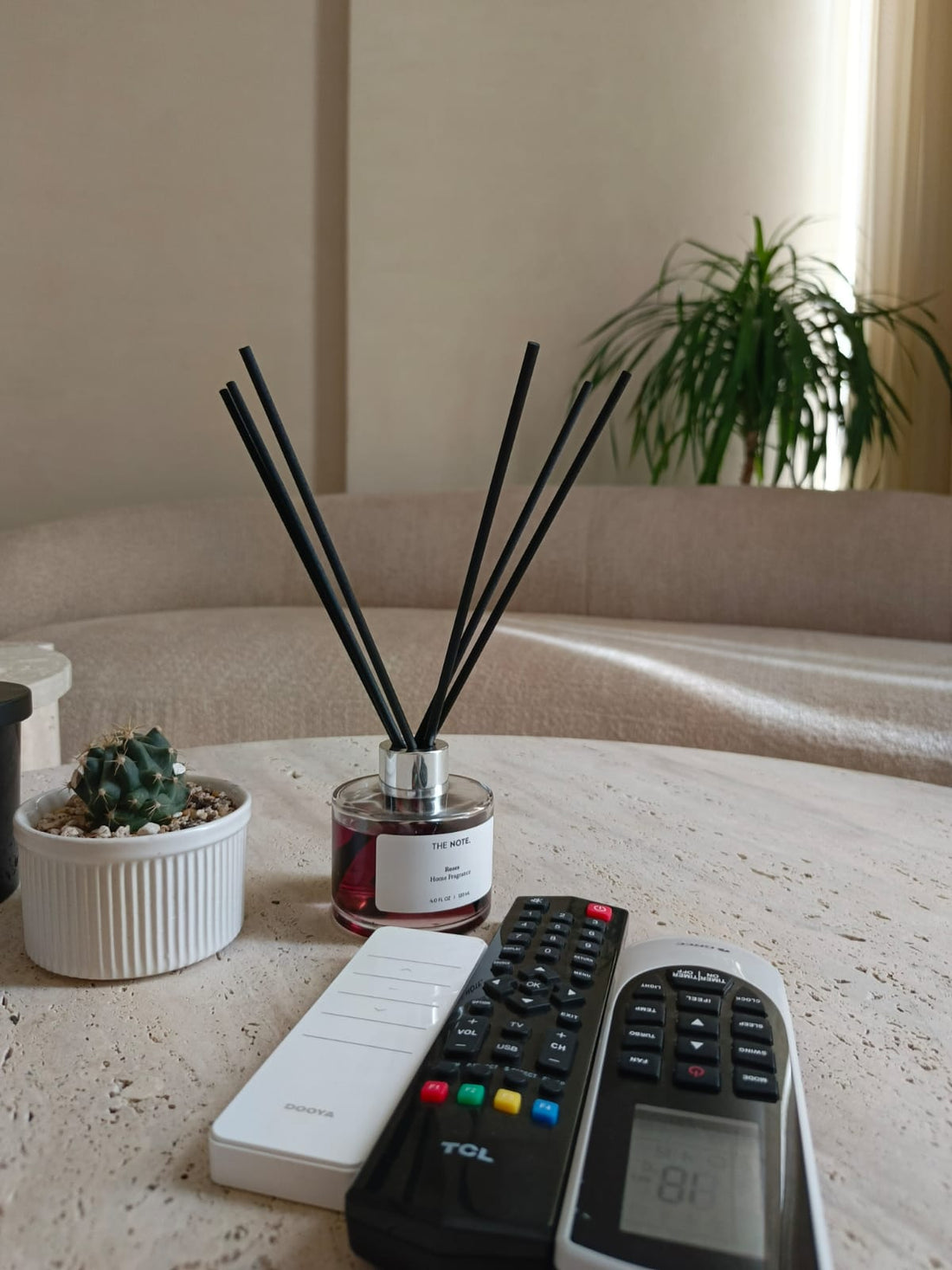 HE NOTE reed diffuser placed elegantly on a wooden coffee table next to flowers and books