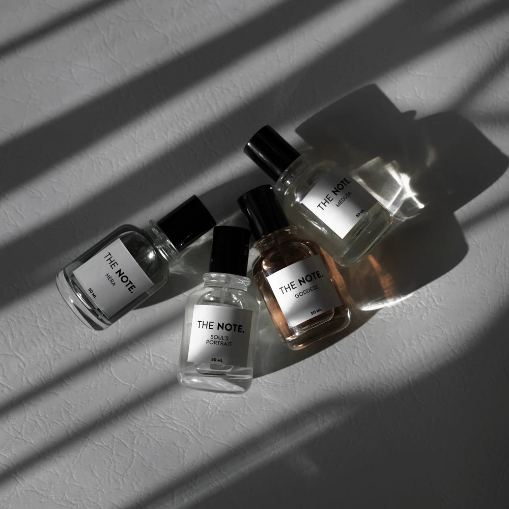 THE NOTE women's perfumes collection including Hera, Soul's Portrait, Goddess, and Medusa – elegant 50ml bottles displayed on textured white surface with natural shadows.